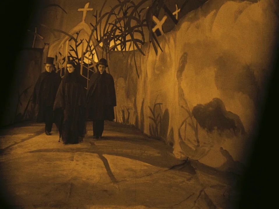 The Cabinet of Dr. Caligari (1920) movie still: fullbody — A theatrical set design with stylized painted backdrops of crosses and twisted skeletal…