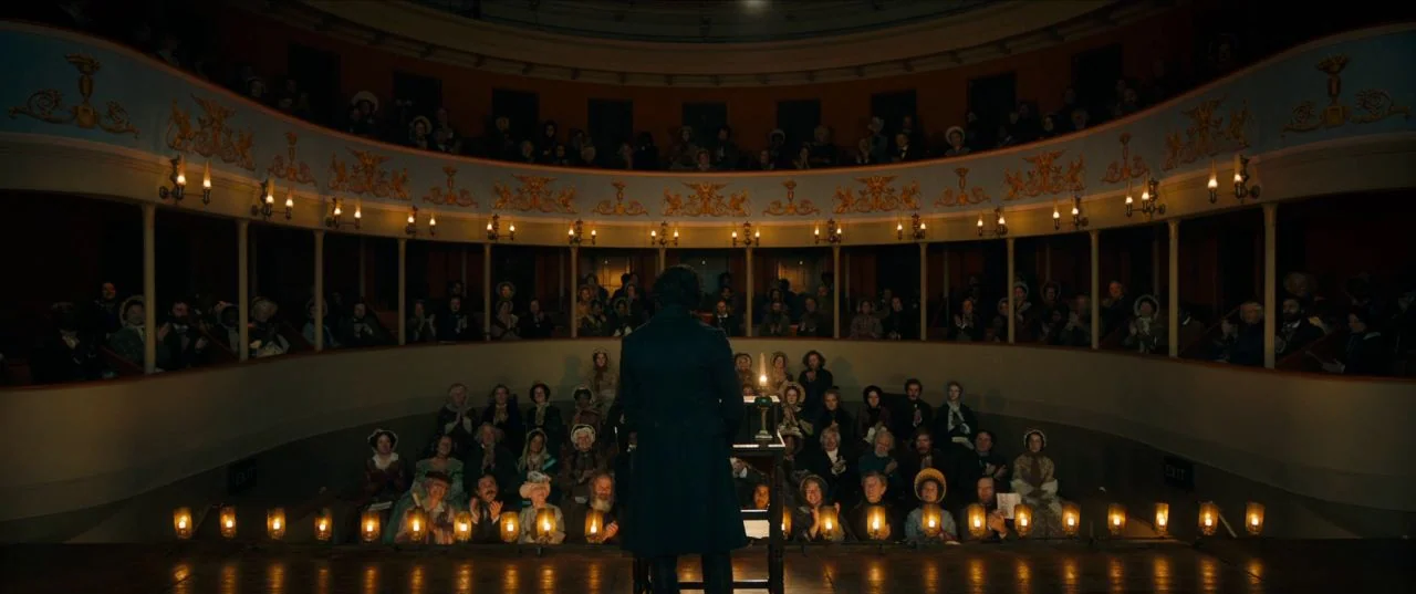 The Personal History of David Copperfield (2019) movie still: wide — A historic theater interior with multiple balconies and dim rows of flickering…