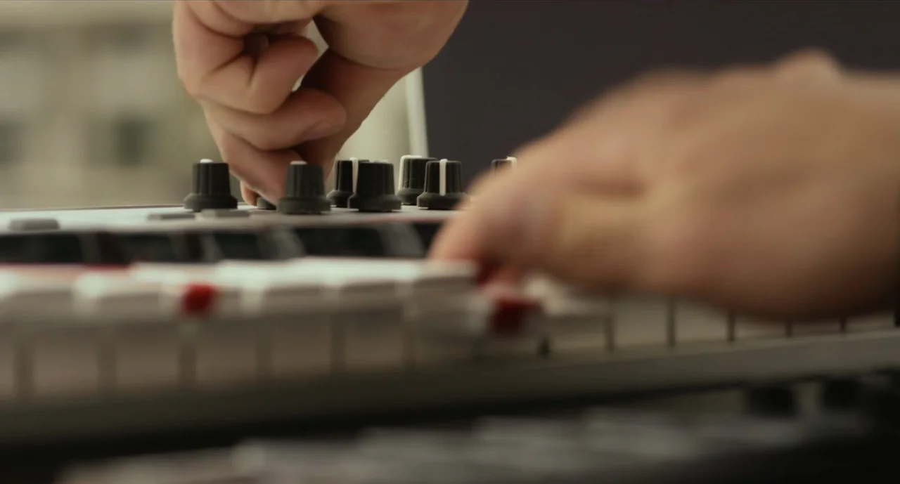 We Are Your Friends (2015) movie still: closeup — A workspace features a MIDI keyboard controller with white keys and black knobs. Two human hands…