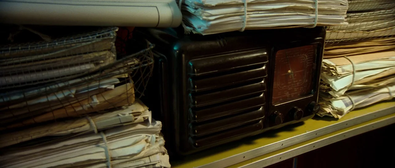 Ip Man 2 (2010) movie still: closeup — A cluttered shelf holds a vintage dark brown radio surrounded by stacks of papers. The documents are bundled…