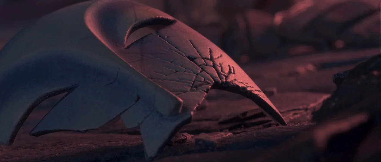 Kubo and the Two Strings movie still: closeup — A cracked white mask lies face down on a dark, textured ground surface. The scene is illuminated by…