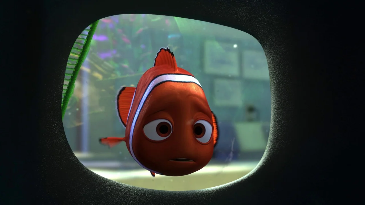 Finding Nemo (2003) movie still: closeup — A clownfish swims inside a glass enclosure looking toward the exterior. The blurred room background…