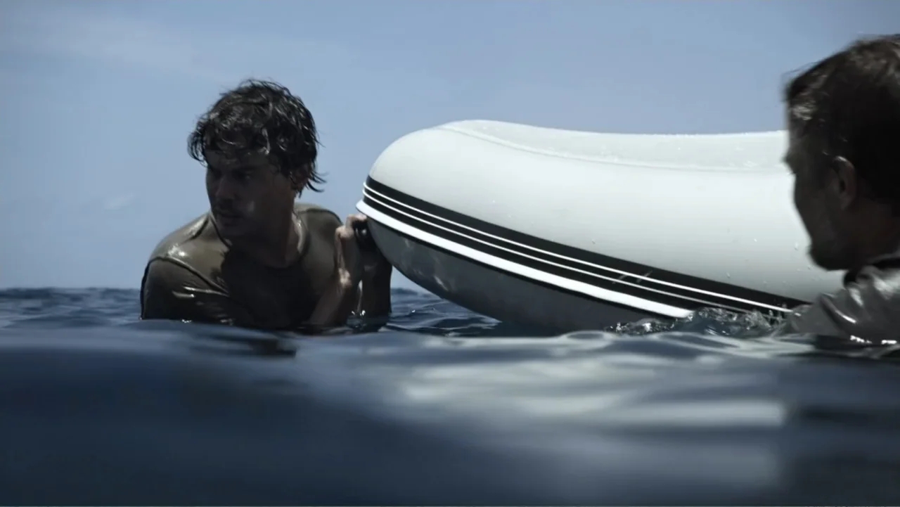 Capsized: Blood in the Water (2019) movie still: medium — Two men are in the middle of a vast, deep blue ocean surface. They both grip a white…