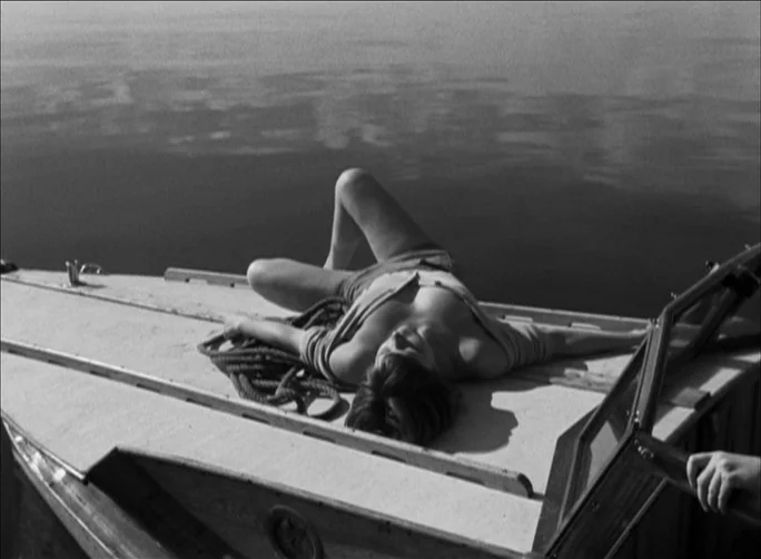 Summer with Monika (1953) movie still: medium — A woman lies on the wooden deck of a motorboat floating on calm water. The sun casts a sharp shadow…