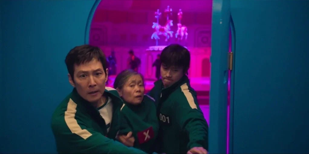 Squid Game (2024) movie still: medium — A teal-colored corridor archway frames a magenta-lit room featuring a central rotating carousel. Three…