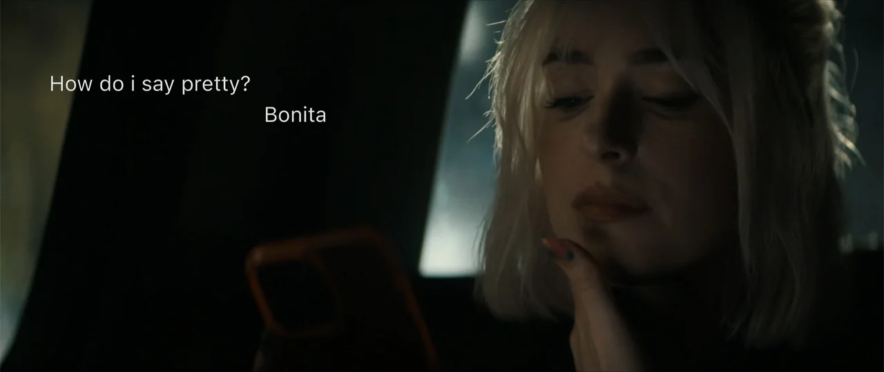 Daddio (2024) movie still: closeup — The interior of a vehicle at night is dark with shadows. A young woman looks at her smartphone screen which…