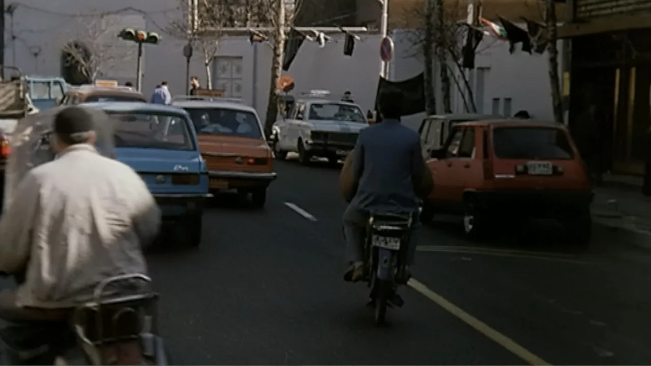 The Mirror (2014) movie still: medium — A crowded city road features several vintage automobiles and two people on motorcycles. A man on a…