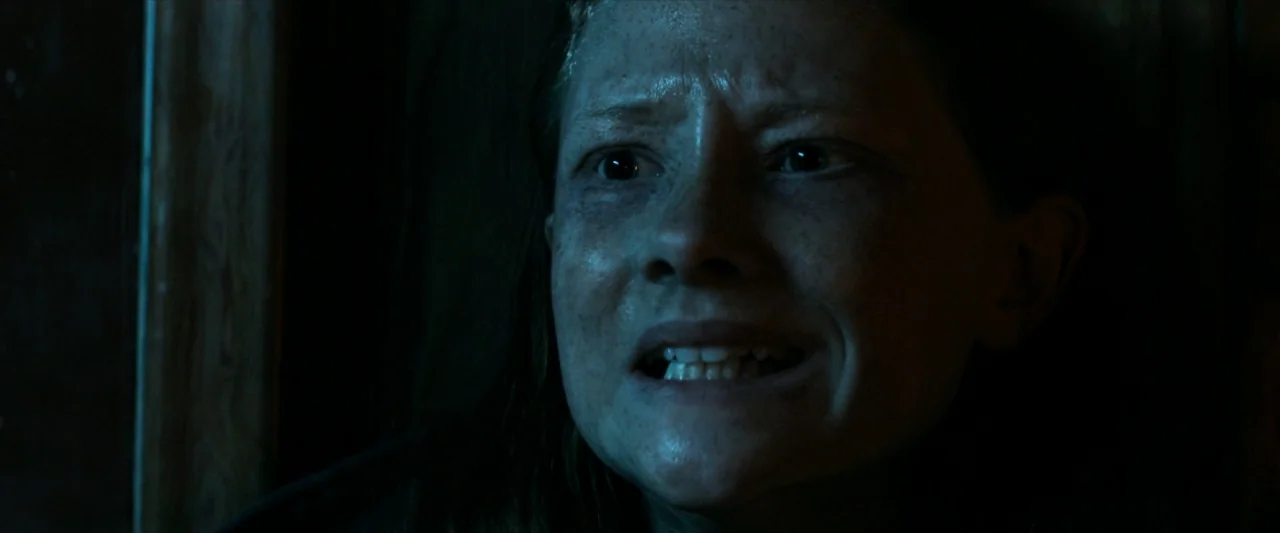 The Silencing (2020) movie still: closeup — A person is situated in a dark, confined space with minimal visibility. The individual looks toward the…