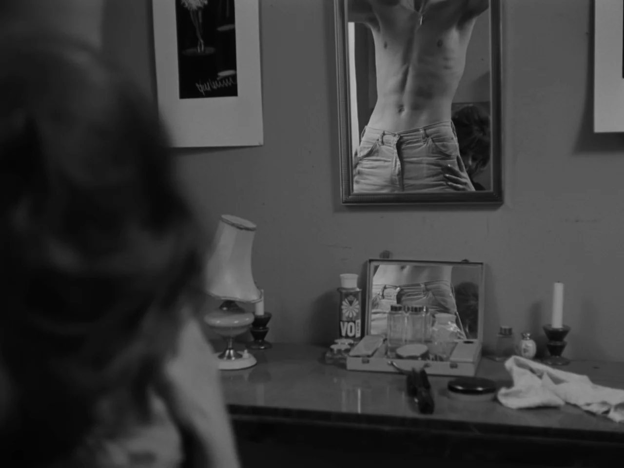 The Baby Carriage (1963) movie still: medium — A vanity table sits in a room with a mirror reflecting a man's torso. Various toiletries, a lamp, and…