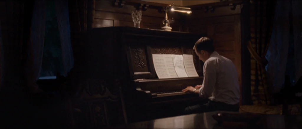 The Killer Inside Me (2010) movie still: medium — A dark wooden study features an upright piano topped with a brass desk lamp. A man in a white…