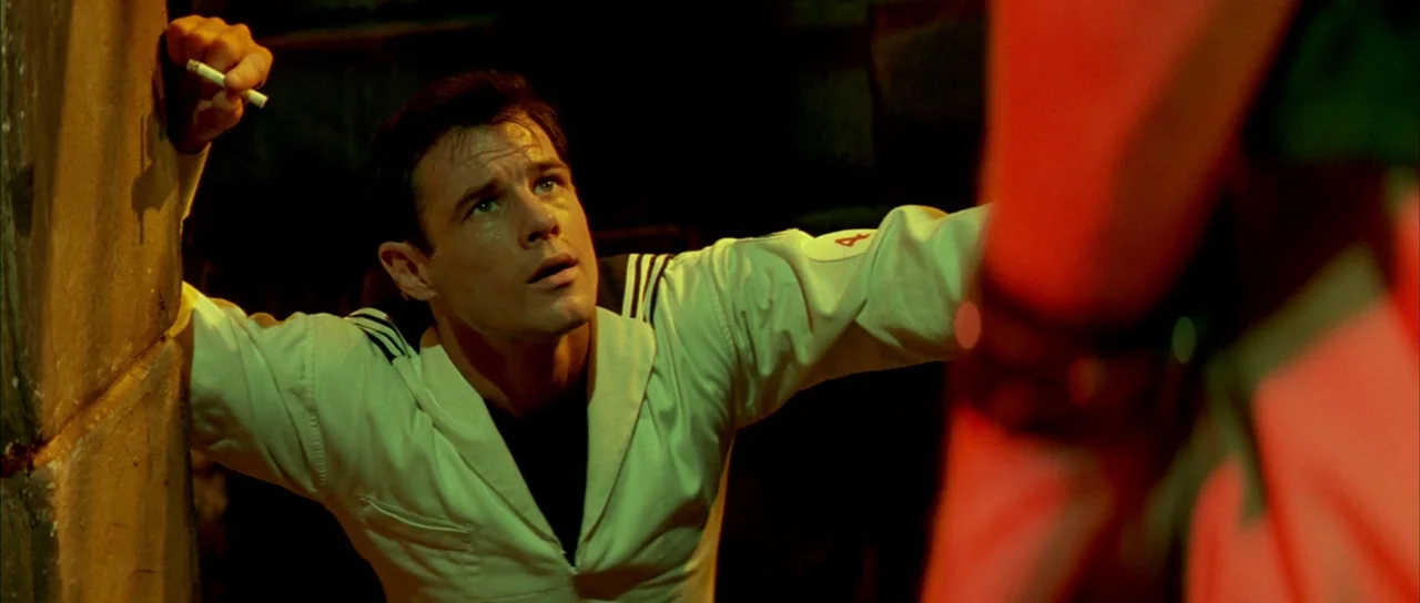 Querelle (1982) movie still: medium — A dimly lit interior compartment on a ship featuring dark pipes and metal bulkheads. A man in a naval uniform…
