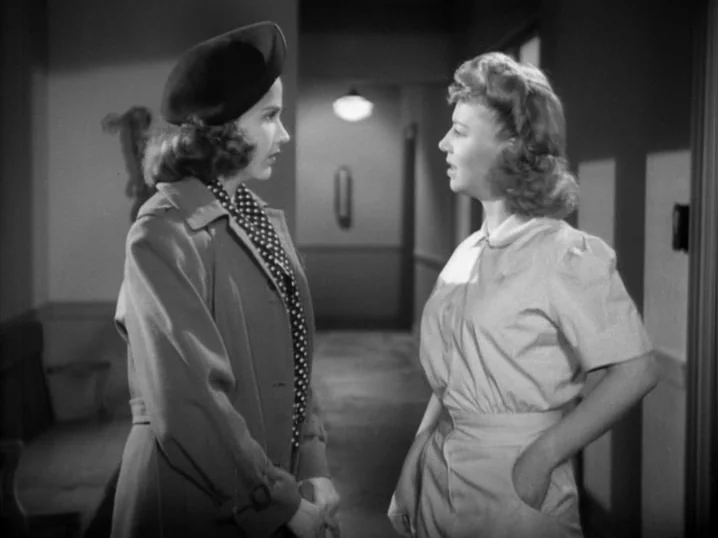 The Seventh Victim (1943) movie still: medium — A hospital hallway features plain walls and a distant ceiling light fixture. Two women stand face to…