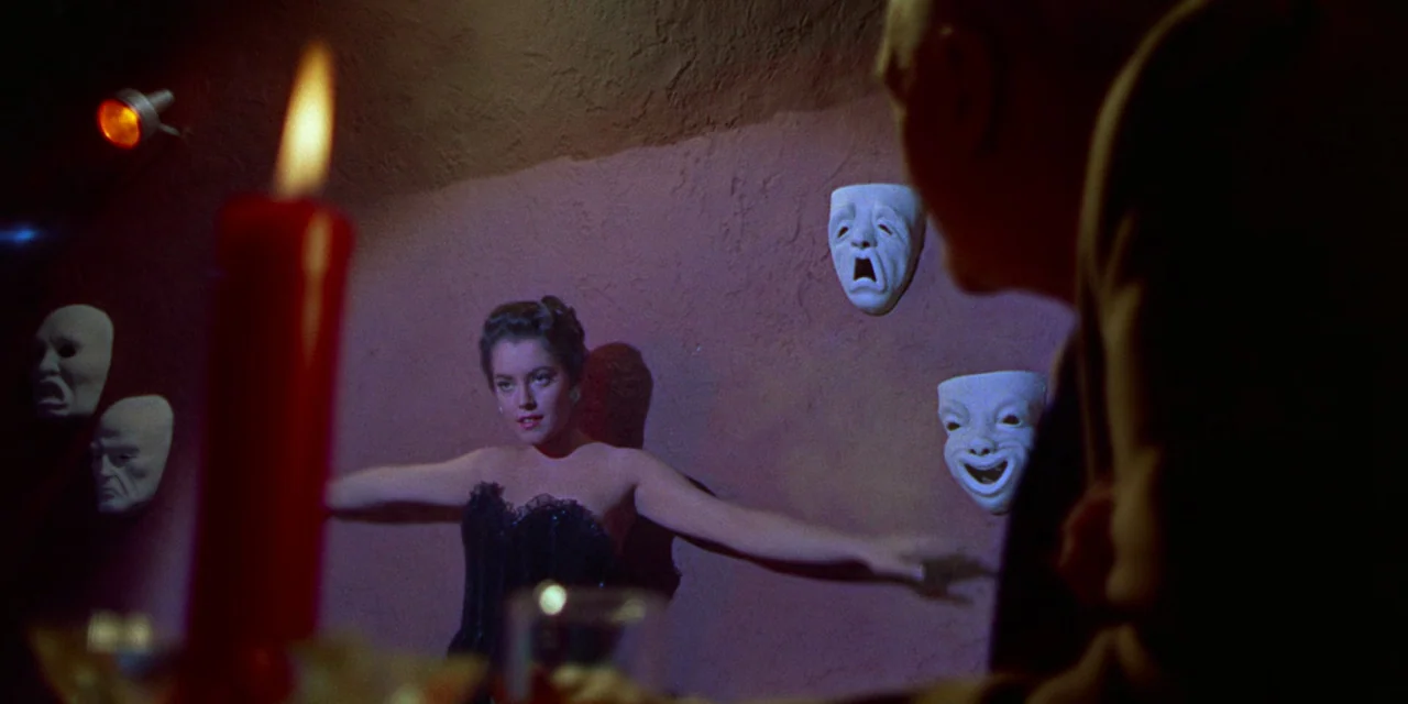 Imitation of Life (1959) movie still: medium — A dimly lit club interior features rough-textured reddish walls adorned with white theatrical masks.…
