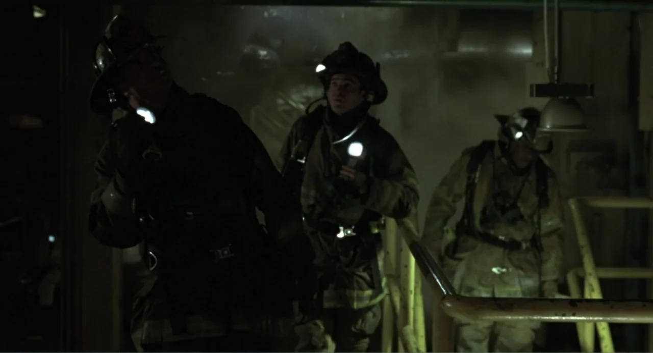 Ladder 49 (2004) movie still: medium — Three firefighters in protective gear descend a dark, dimly lit metal industrial stairwell. They carry…