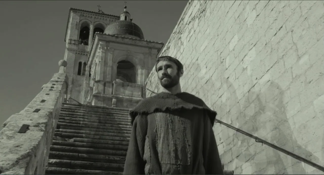 Pope Francis: A Man of His Word (2018) movie still: medium — A stone staircase leads up toward a historic chapel dome under clear daylight. A man in…