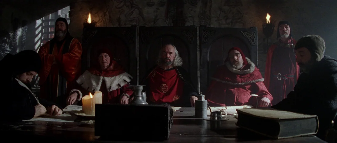 Braveheart (1995) movie still: wide — A dark stone-walled council room is lit by several small candles on a table. Seven men dressed in medieval red…