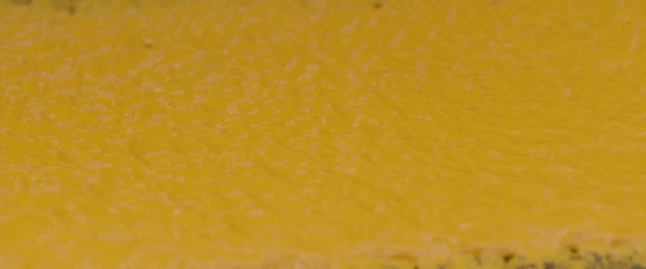 Prince Avalanche (2013) movie still: closeup — A close-up view of a textured yellow-painted surface on an outdoor pavement. The paint shows subtle…