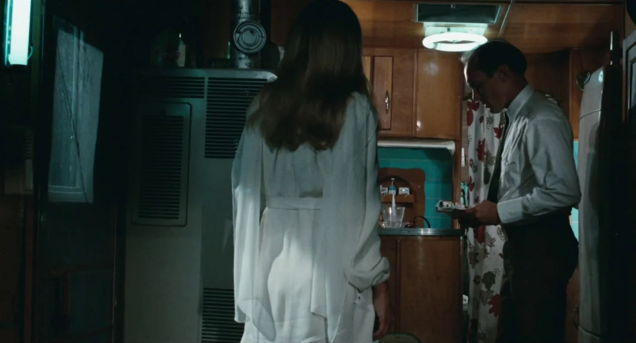 The Rain People (1969) movie still: medium — A cramped interior of a vintage camper with wood paneled walls and floral curtains. A man in a dress…
