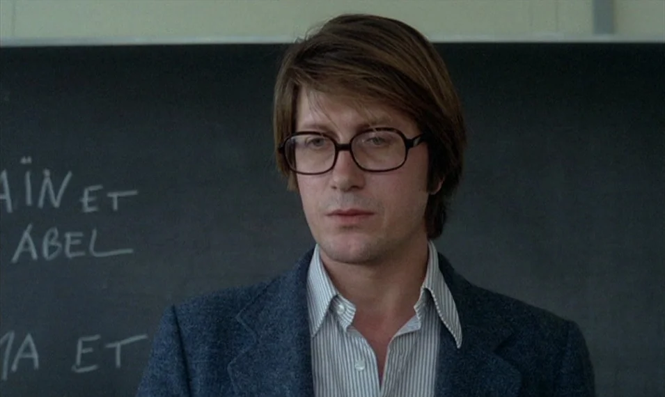 Every Man for Himself (1980) movie still: medium — A man stands before a dark chalkboard with white text written on it. The setting is a classroom…