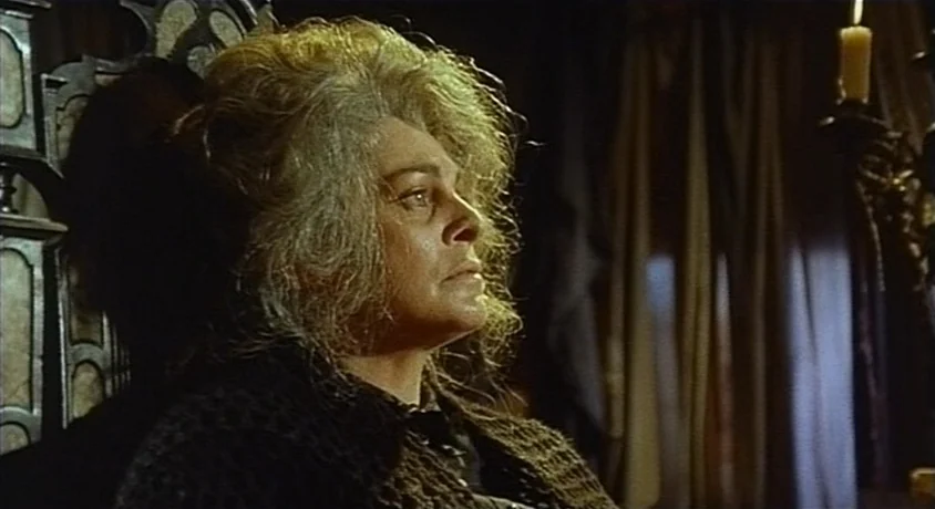 Kill, Baby Kill (1966) movie still: closeup — A dimly lit room features an elderly woman seated against a high-backed wooden chair. Heavy curtains…