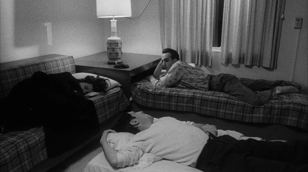 Stranger Than Paradise (1984) movie still: wide — A sparse motel room contains two beds and a lamp on a side table. Three people are positioned on…