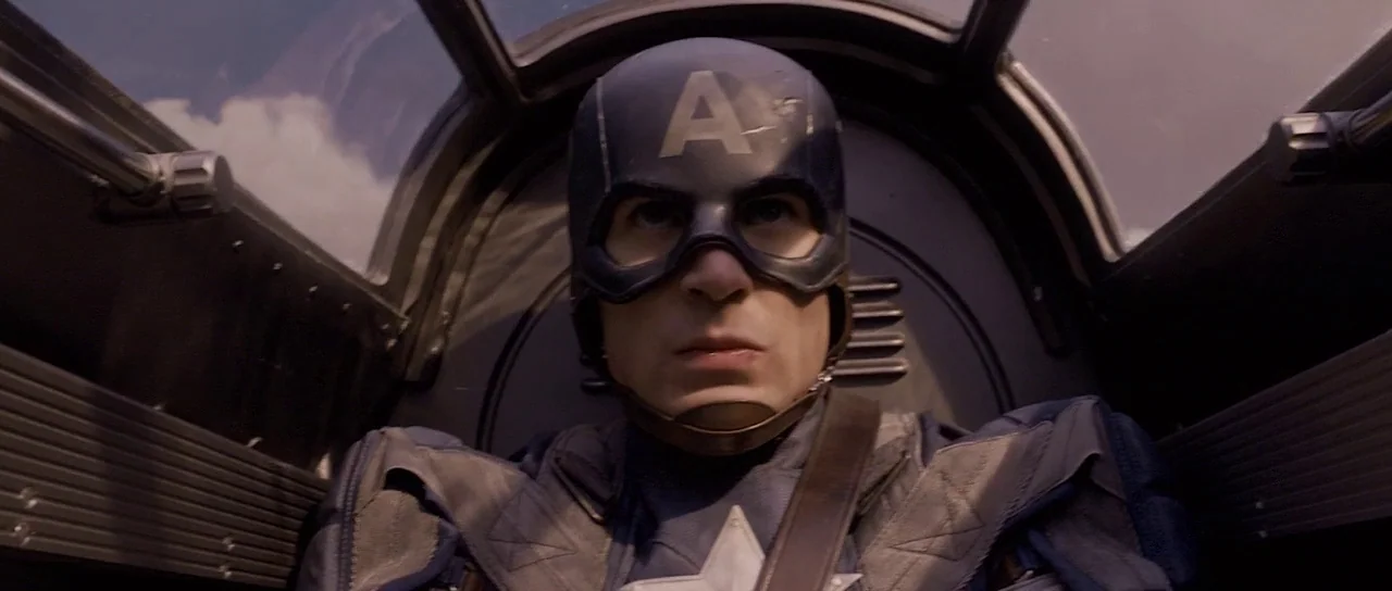 Captain America: The First Avenger (2011) movie still: closeup — A cramped cockpit with metallic walls and a clear overhead glass canopy. A masked…