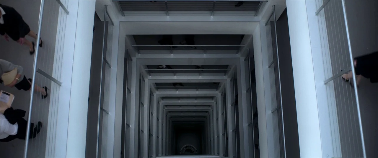 Mayhem (2017) movie still: wide — A modern multi-story atrium with white geometric railings creates a vertical repeating pattern. Multiple…