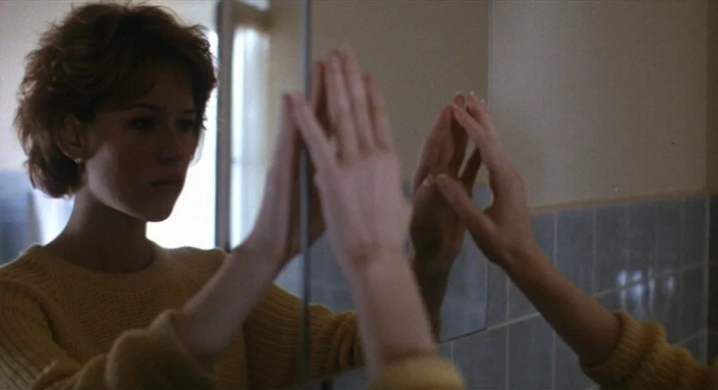 King Lear (1987) movie still: medium — A residential bathroom with light blue wall tiles and a reflective medicine cabinet mirror. A young woman…