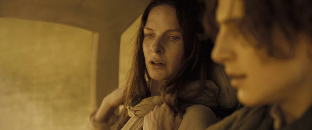 Dune (2021) movie still: closeup — Two individuals sit in a sparsely furnished cabin with light-colored curved walls. The woman faces toward the…