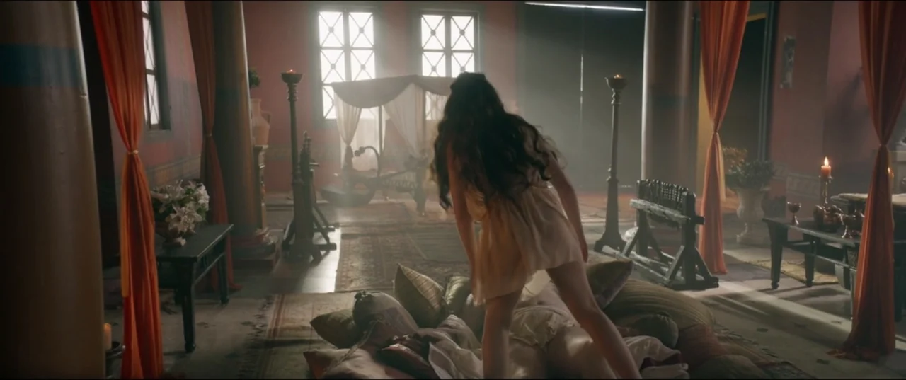 Utopia (2013) movie still: medium — An opulent ancient-style chamber features draped curtains, wooden pillars, and patterned floor rugs. A woman in…