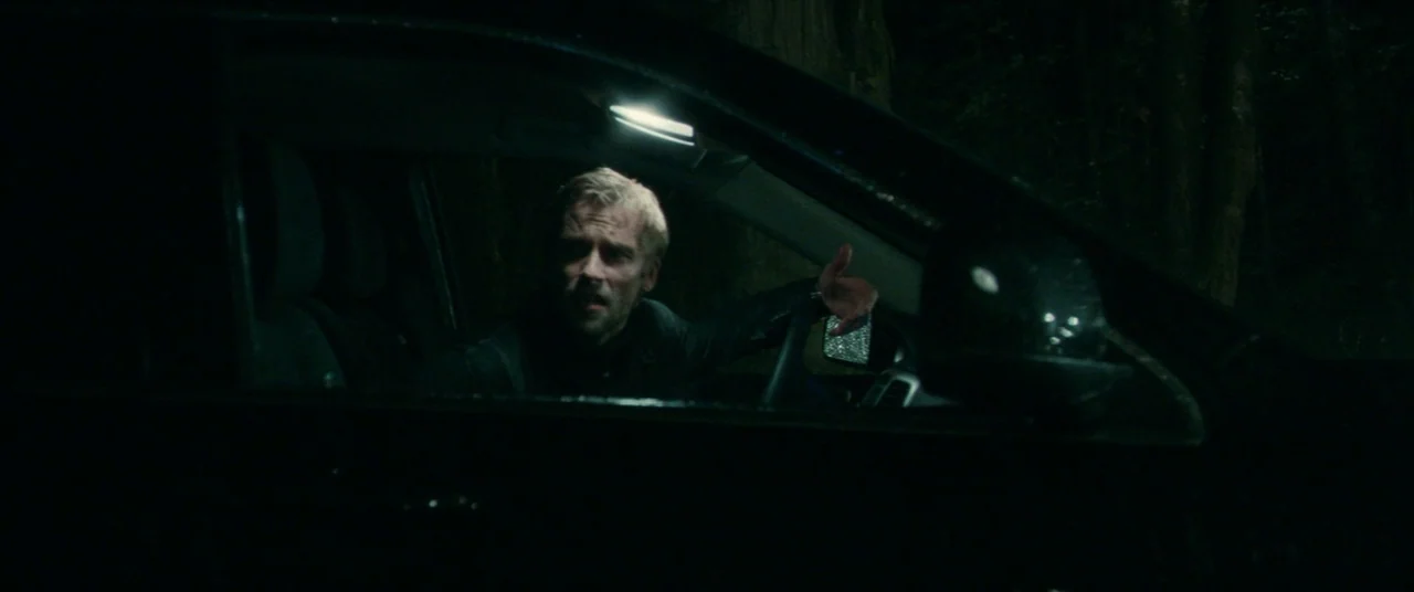 Horns (2013) movie still: medium — A man sits inside a dark vehicle surrounded by the deep shadows of trees. He rests his hand on the steering wheel…