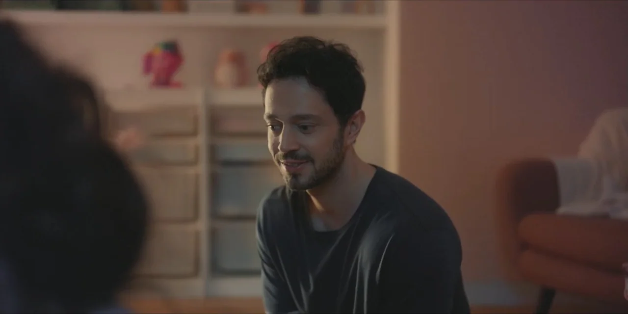Kill Me If You Dare (2019) movie still: medium — A modern living room features shelves filled with toys and a soft colored wall. A man in a dark…