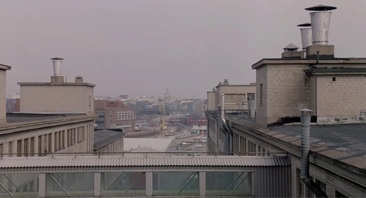 The Match Factory Girl (1990) movie still: establishing — A series of industrial brick building rooftops stretch into an urban distance under…