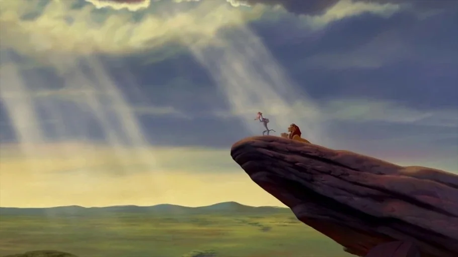 The Lion King (1994) movie still: wide — A high rocky promontory overlooks a vast, flat grassland savanna under a cloudy sky. A mandrill stands at…