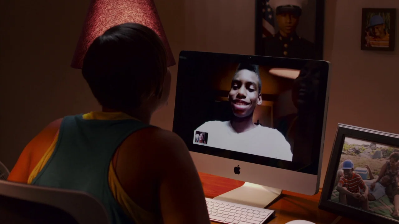 Red Hook Summer (2012) movie still: medium — A dimly lit room contains a computer desk with framed photos and a lamp. A woman sits in front of her…