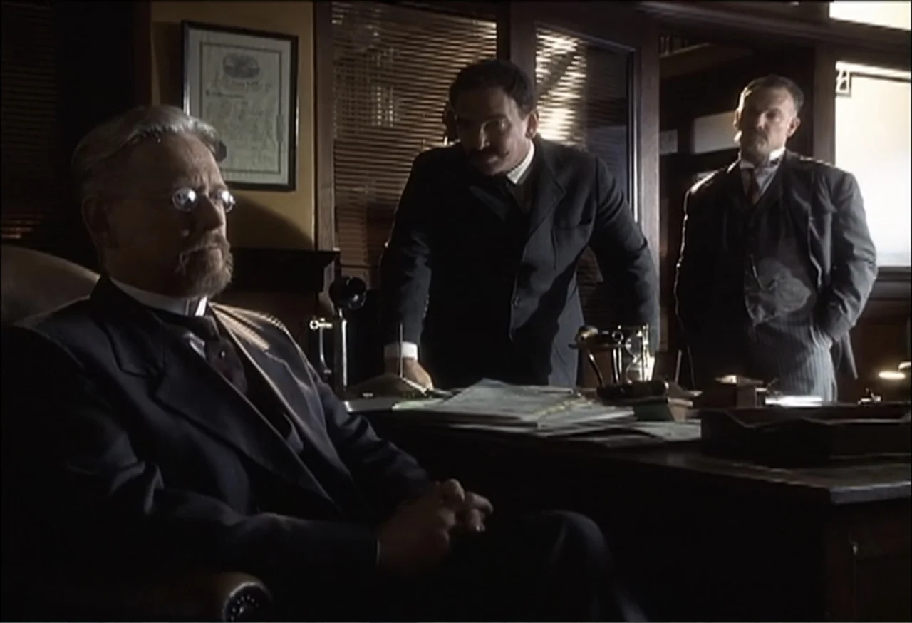 Vendetta (2022) movie still: medium — A 1900s wood-paneled office contains a heavy desk with papers and a telephone. Three men in formal suits stand…