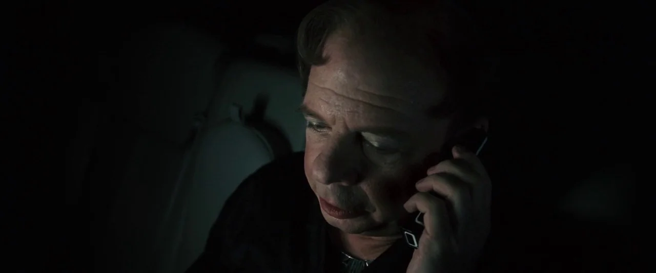 Southland Tales (2006) movie still: closeup — A man sits in the dark interior of a vehicle at night. He holds a glowing mobile device against the…