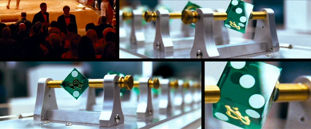 Ocean’s Thirteen (2007) movie still: closeup — A close-up split-screen showing green dice mounted on gold rods in a technical space. The mechanism…
