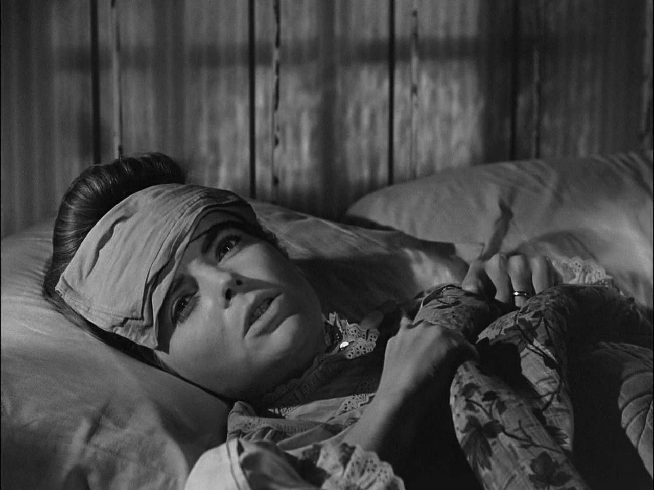 A Tree Grows In Brooklyn (1945) movie still: closeup — A dark, wood-paneled room contains a bed with pillows. A young woman lies resting with a…