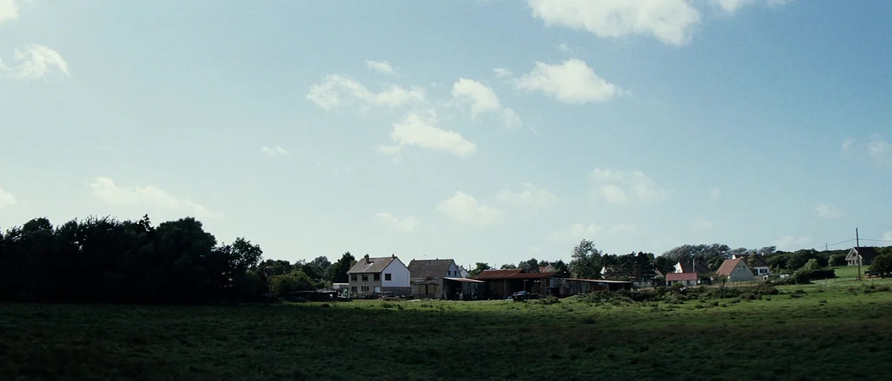 Outside Satan (2011) movie still: establishing — A rural expanse features scattered houses and farm buildings nestled among trees. Green fields…