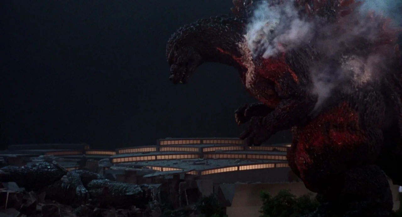 Godzilla vs. Destoroyah (1995) movie still: wide — A massive monster stands in a dark landscape filled with rubble and burning structures. The…
