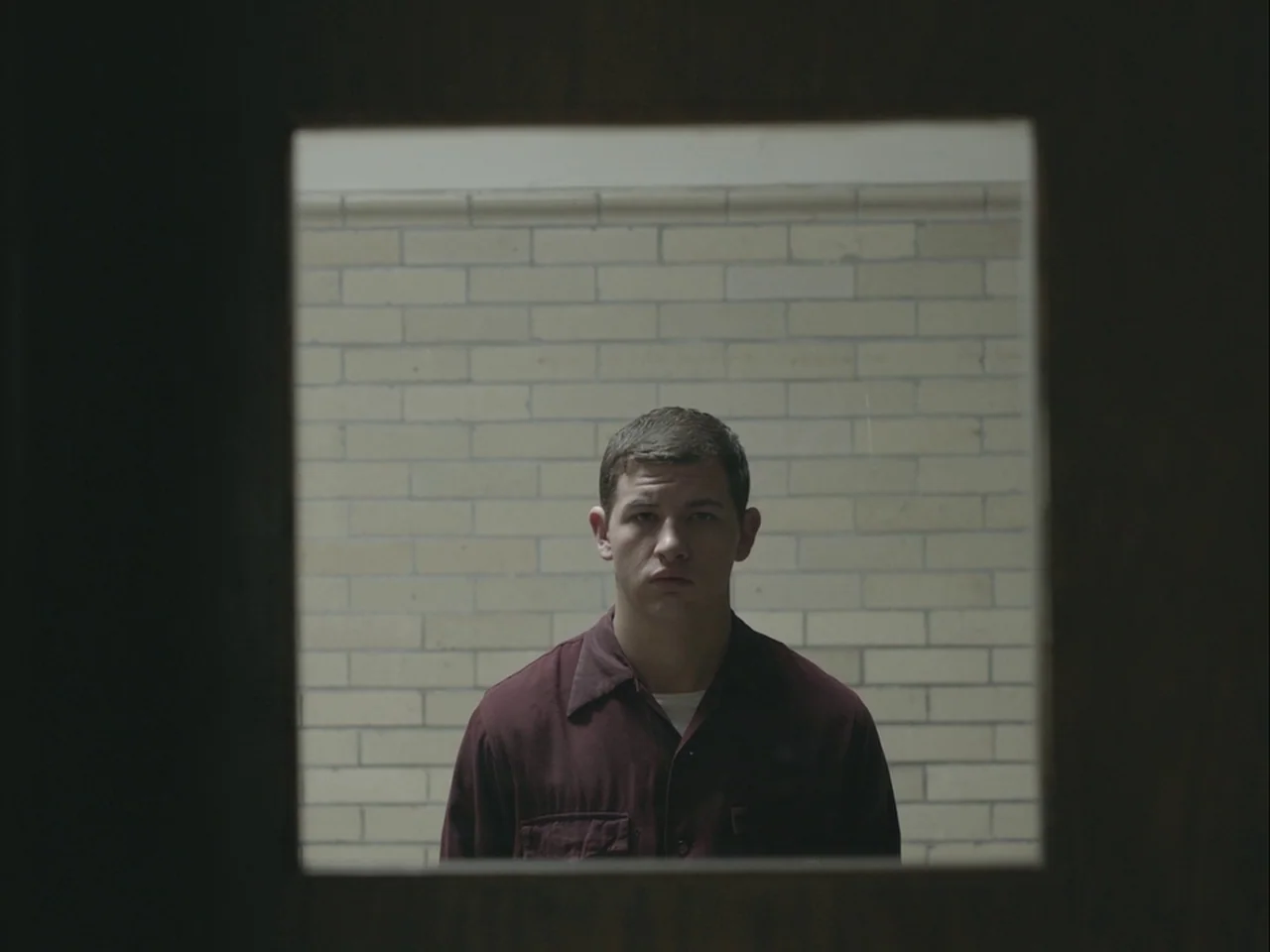The Mountain (2018) movie still: medium — A light-colored brick wall serves as the backdrop behind a man. The subject looks directly into the lens…
