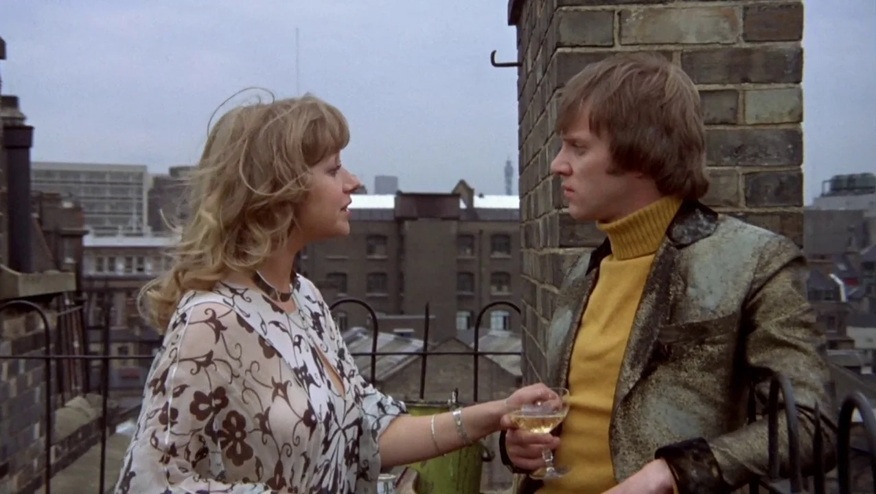 O Lucky Man! (1973) movie still: medium — Two individuals stand together on an urban rooftop during a cloudy day. The woman talks to the man while…