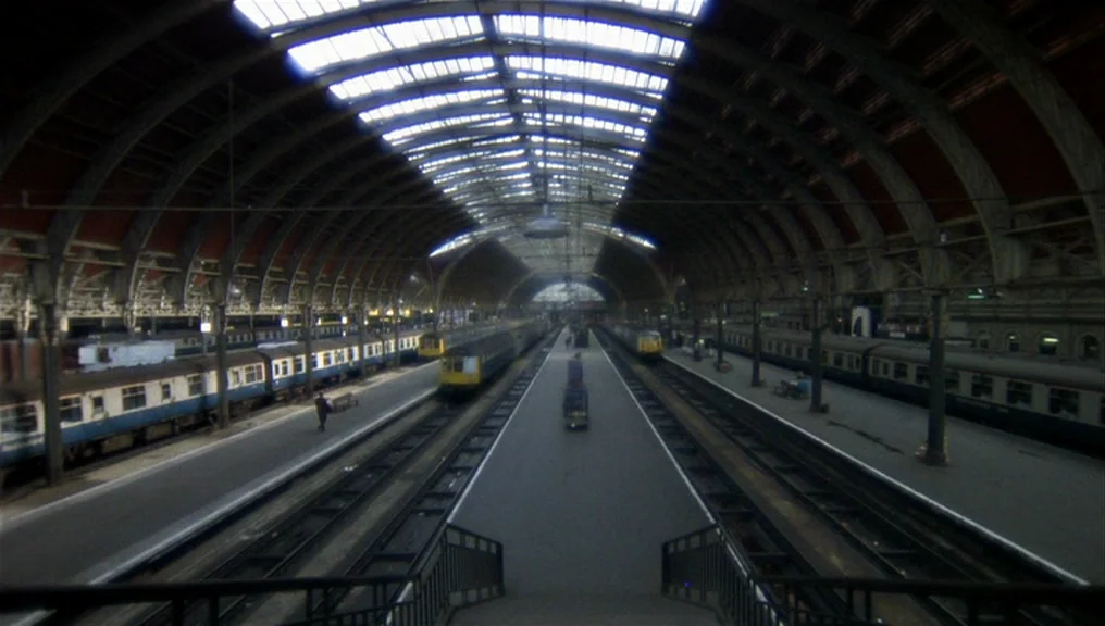 Performance (1970) movie still: establishing — A vast, Victorian-style iron and glass railway terminal features multiple tracks and stationary…