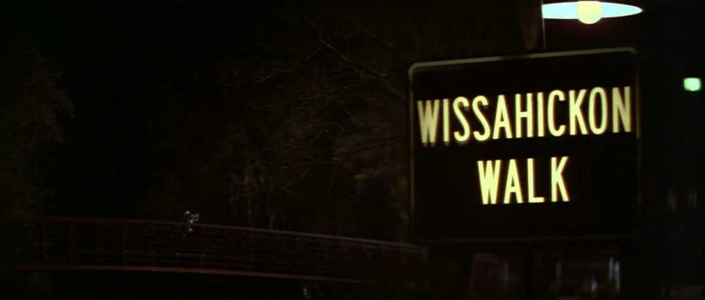 Blow Out (1981) movie still: establishing — A dark outdoor space at night contains a brightly lit directional park sign. The sign reads Wissahickon…