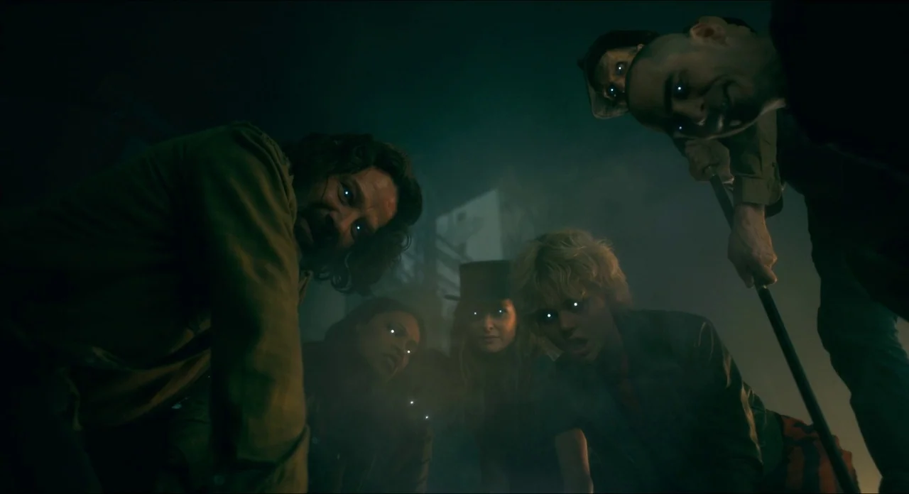 Doctor Sleep movie still: medium — A dark, hazy alleyway features five individuals gathered in a tight, downward-facing huddle. The figures look…