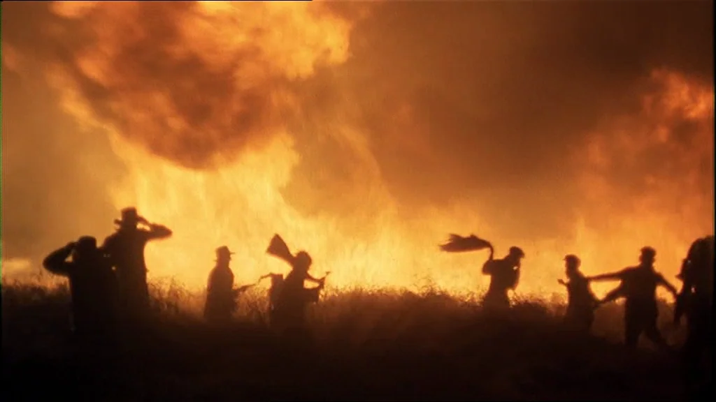 Days Of Heaven (1978) movie still: wide — A field of tall grass is engulfed in massive orange flames at night. Several silhouetted figures move…
