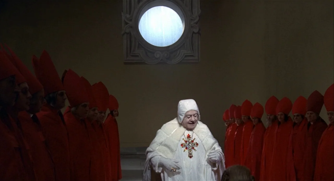 Fellini’s Casanova (1976) movie still: fullbody — A spacious interior room features high walls and a single circular window above. A central figure…