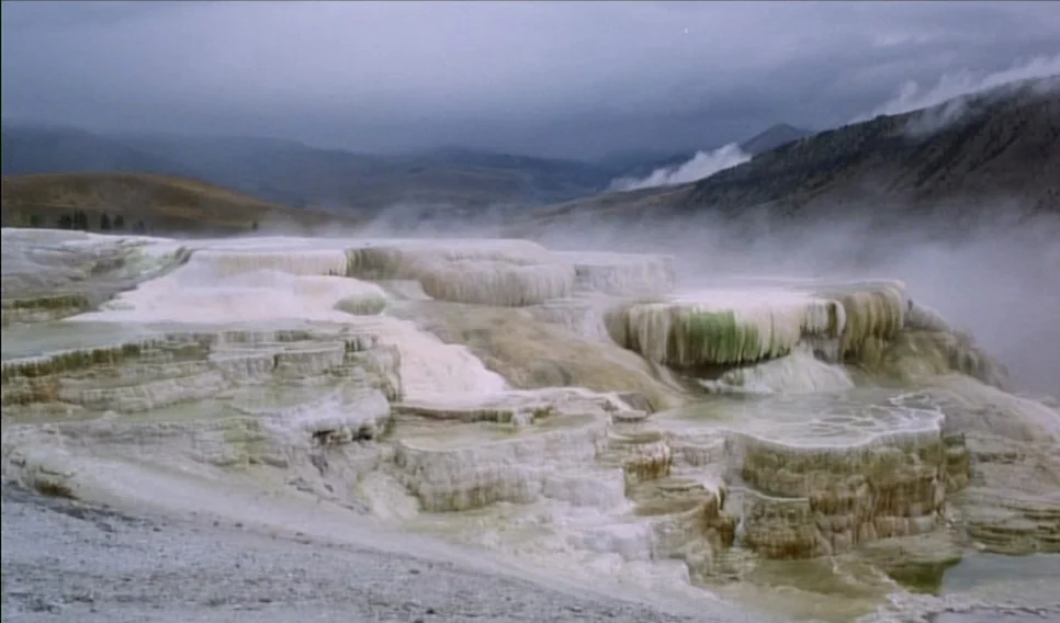 Heart of Glass (1976) movie still: wide — A vast geothermal landscape features tiered white mineral terraces with pools of water. Thick steam drifts…