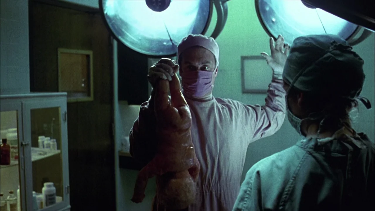 Addams Family Values (1993) movie still: medium — A dark hospital room contains a doctor holding a newborn infant in the air. The room features…